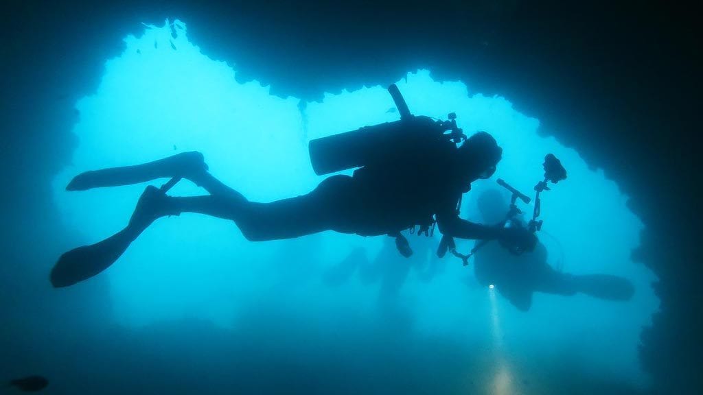 Divers silhouetted on one of the caves at ko dok mai diving phuket diveplanit