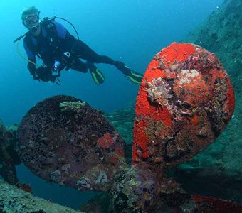Scuba diver posing above the propellor of a wreck